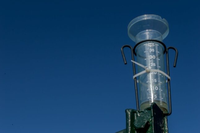 Pluviometer or rain gauge on a clear blue sky background with some rainwater. Instrument used in meteorology to calculate the amount of rain per cubic meter.