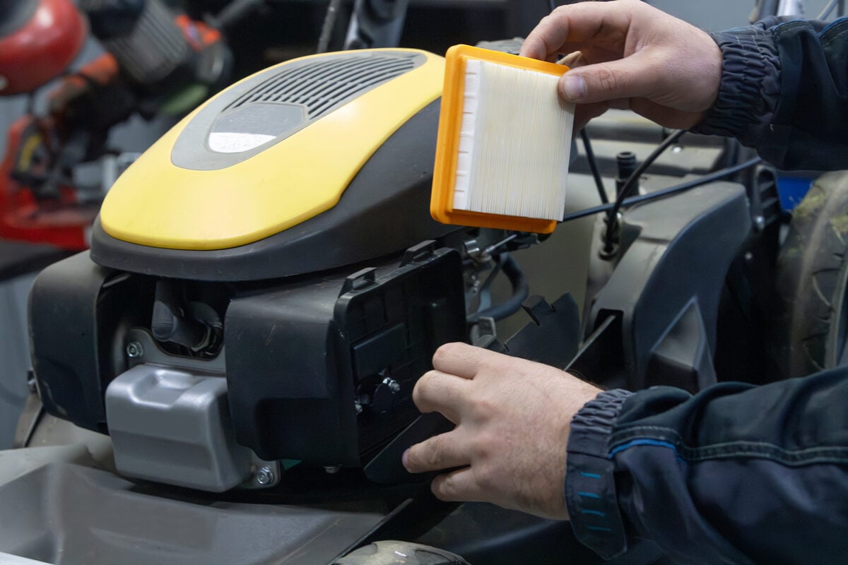 person replacing the air filter on a black lawn mower using his hand
