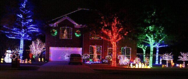 Holiday decorations at night, lighted trees, window lights, roof lights, lighted figures on the grass, all sorts of colors