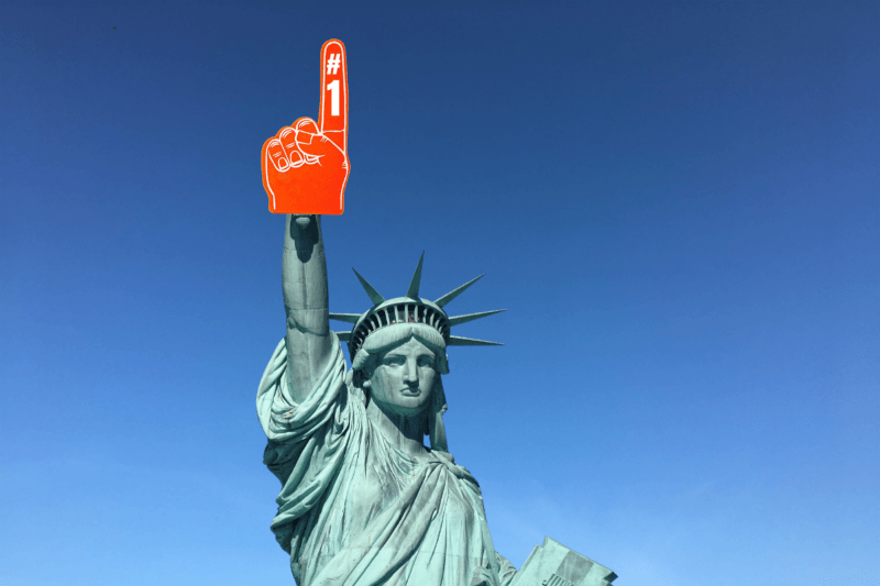 The Statue of Liberty waves an orange foam finger with a “#1” to indicate its dominance in LawnStarter and Home Gnome city rankings.