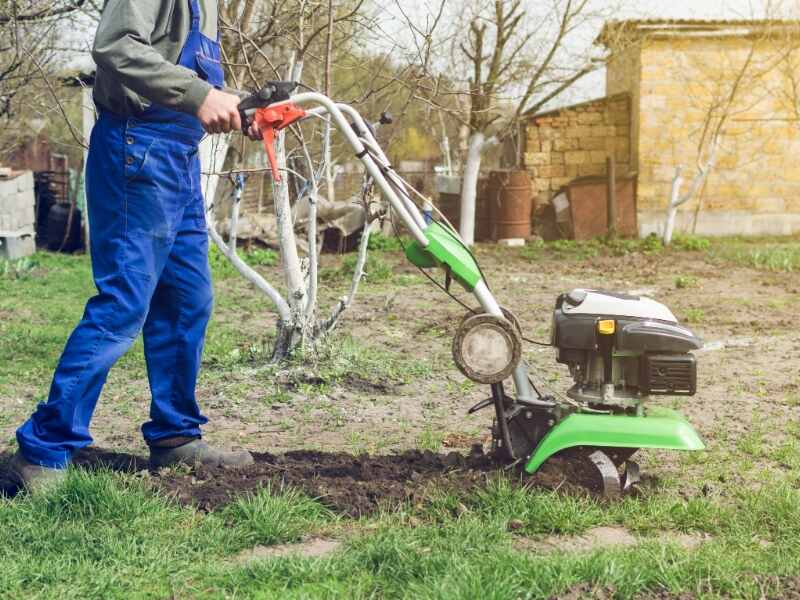 Man in overalls pushing green grass tiller across open ground