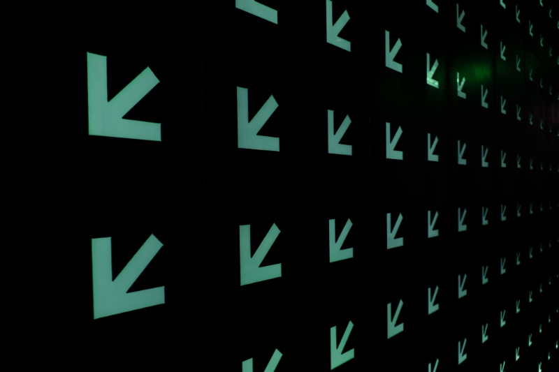 Glowing green arrows repeat across a black wall at SXSW headquarters, receding into the distance in a dim hallway.