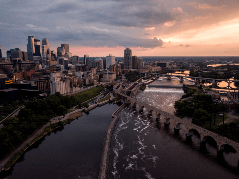 An aerial view of the Minneapolis, Minnesota, skyline at sunset, with the Mississipi River in the foreground