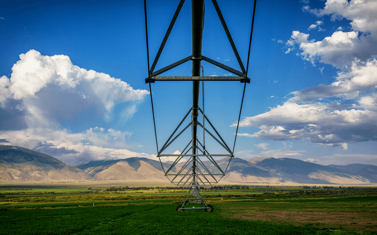 A farm irrigation system stands above a green crop field with mountains in the distance
