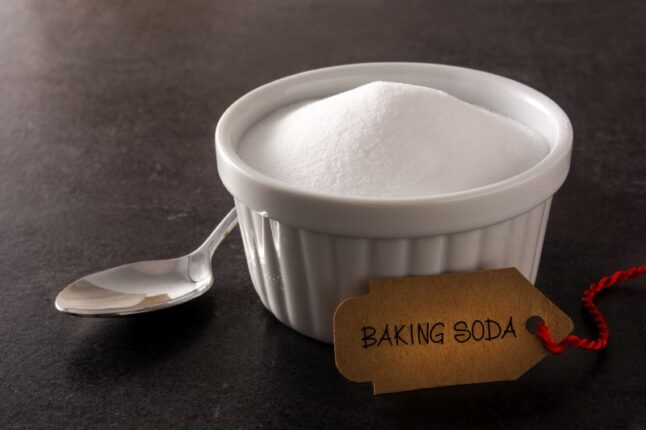 A small bowl of baking soda with a teaspoon and a tag next to it