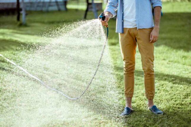Man watering green lawn, sprinkling water on the grass with water pistol, close-up with no face