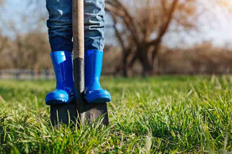 Close up of childs feet in rubber boots on shovel