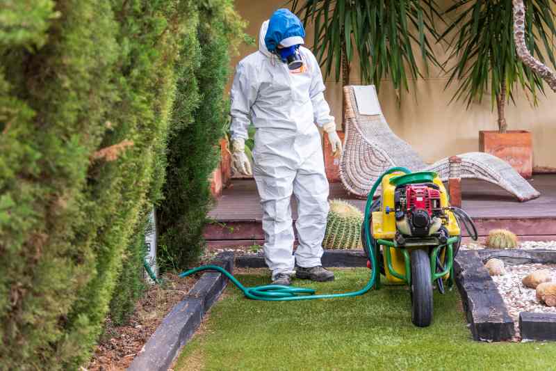 Person in protective gear with a machine sprayer on a lawn