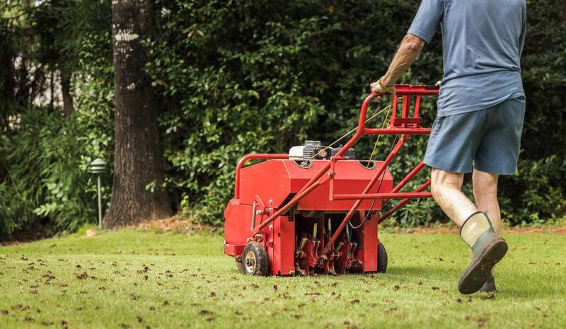 Man using gas powered aerating machine to aerate residential grass yard.