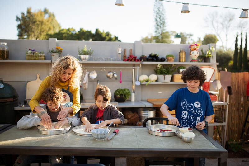 Mother teaching boys kneading pizza dough on table in backyard