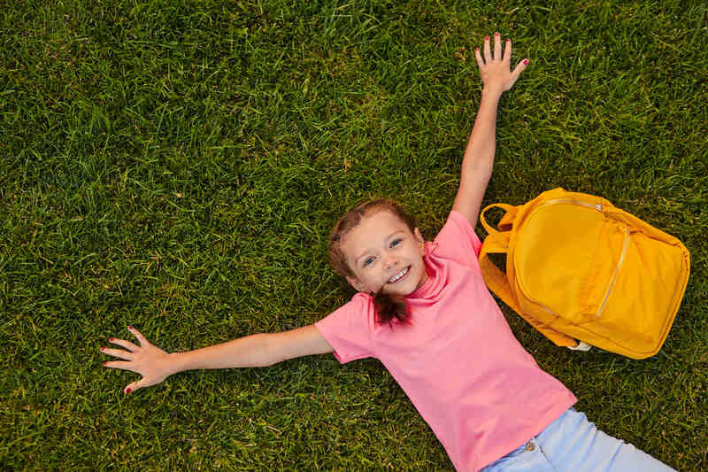 Smiling young girl lying on grass with backpack