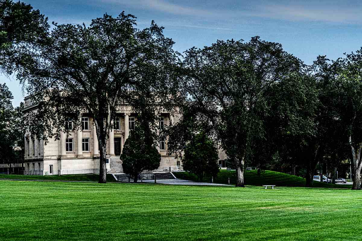 Green lawn and leafy trees outside a classical stone government building in Bismarck, North Dakota, under a clear blue spring sky.