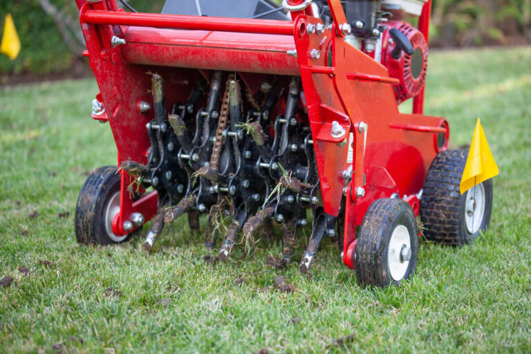 A red aerator on a lawn between yellow flags