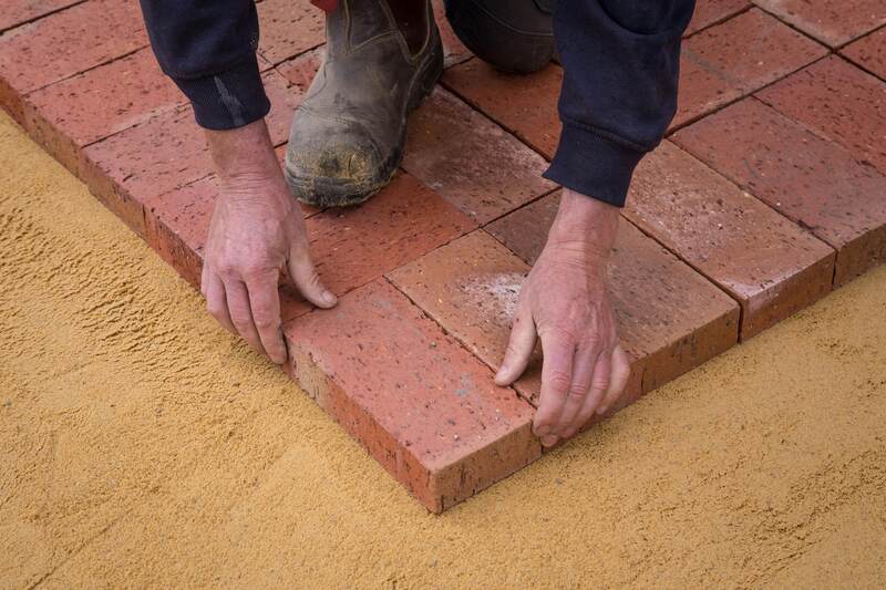 Worker laying red brick pavers