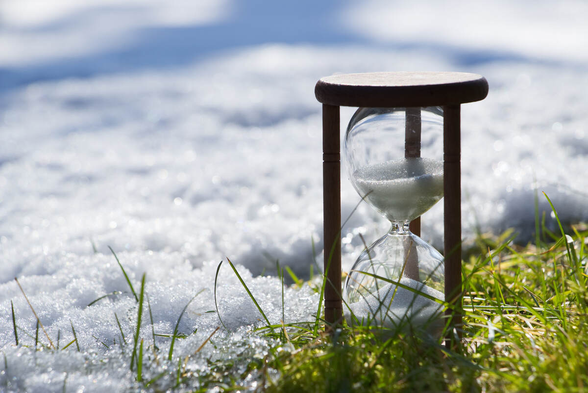 Hourglass sitting on snow-covered winter grass.