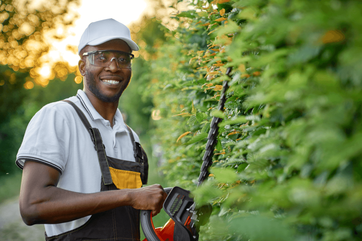 A landscaper smiles while trimming hedges.
