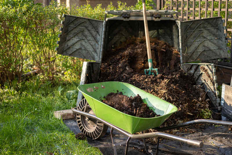 compost bin opened up with pitchfork and wheelbarrow nearby