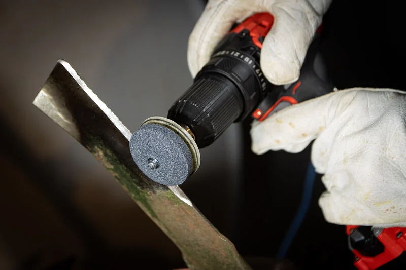Lawnmower blade being sharpened with drill attachment.