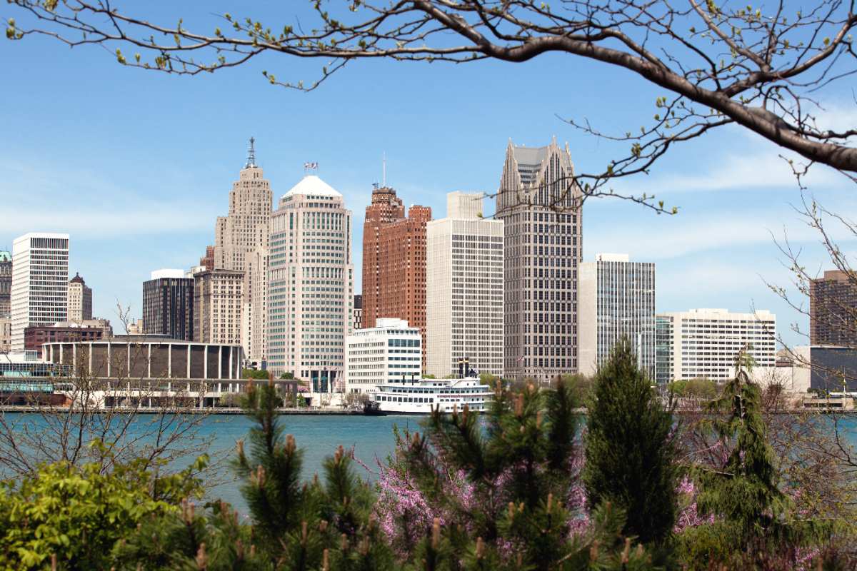 Detroit skyline viewed across the river with budding branches and early spring blossoms in the foreground, signaling the arrival of warmer weather.