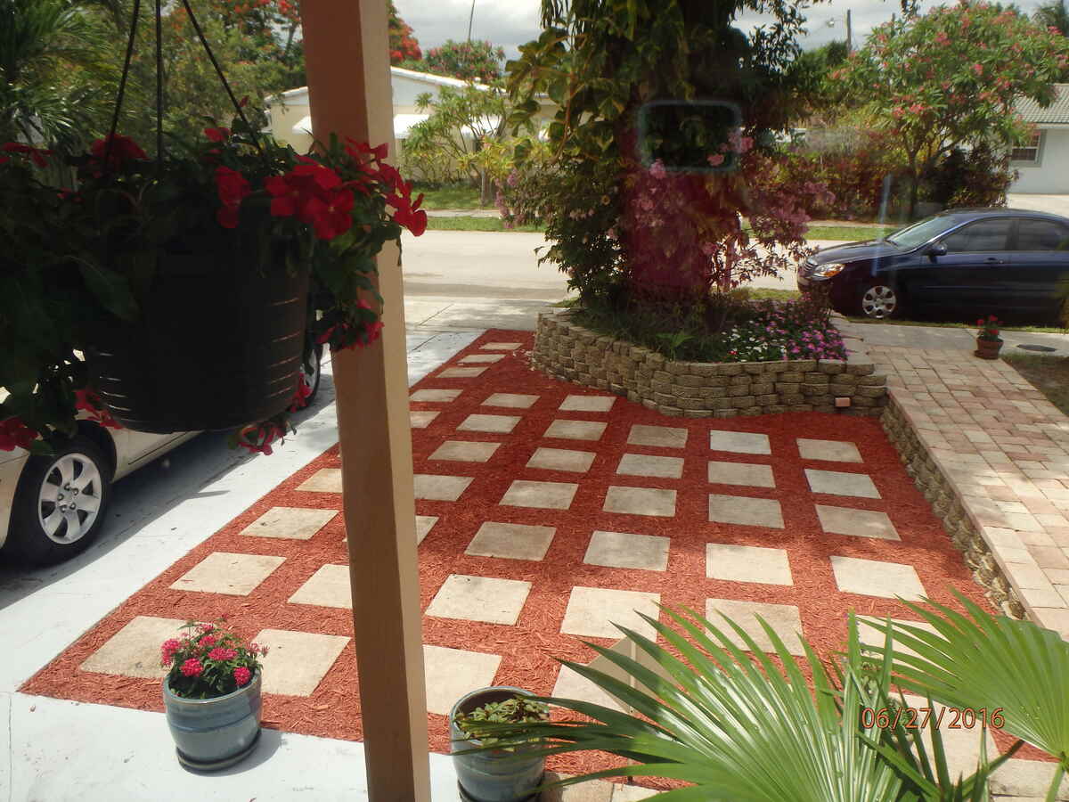 Red mulch surrounds square, light-gray pavers in this ground-level shot. The pavers are arranged in a grid, and the red mulch provides a contrasting background.