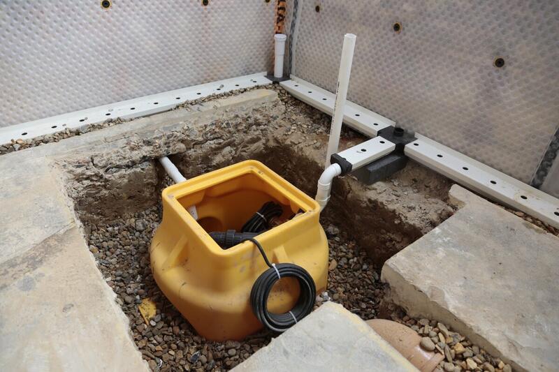 Indoor sump pump basin installed in a gravel pit with connected drainage pipes, used for basement waterproofing and groundwater management.