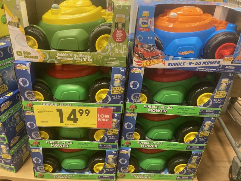 Stack of colorful “Bubble ‘N’ Go Mower” toy lawn mowers on a store shelf, priced at $14.99. The toys are designed for kids and blow bubbles as they’re pushed, mimicking a real lawn mower. Each box includes a small bottle of bubble solution and indicates no batteries are required.