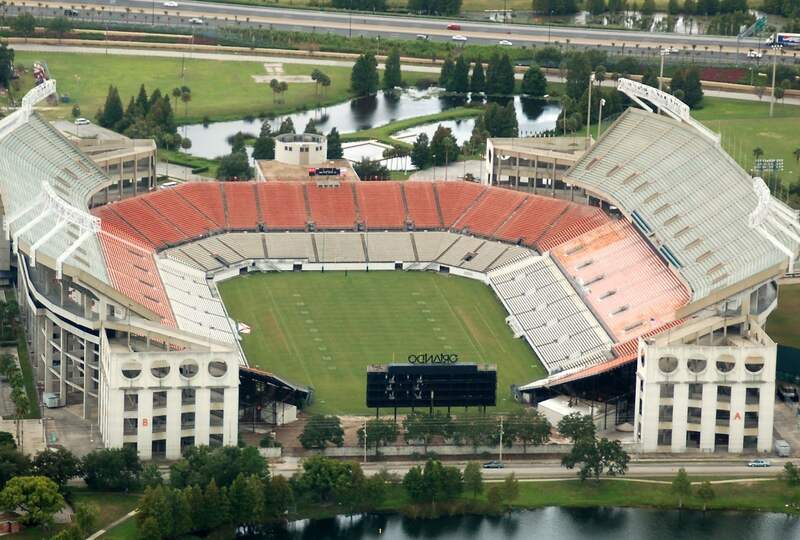 Aerial view of empty Camping World Stadium in Orlando, surrounded by water and greenery.