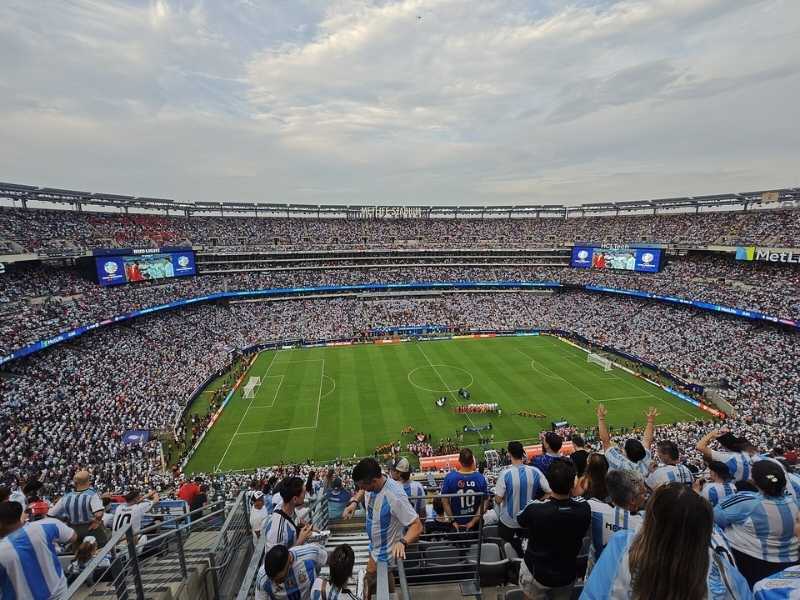 Packed MetLife Stadium crowd cheering during Argentina soccer match, banners and flags waving.