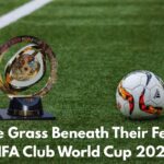 A FIFA Club World Cup trophy and an Adidas soccer ball sit on a lush green stadium field. Bold white text at the bottom reads: “The Grass Beneath Their Feet: FIFA Club World Cup 2025.”