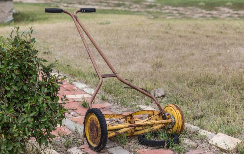old vintage antique manual push mower with a broken wheel