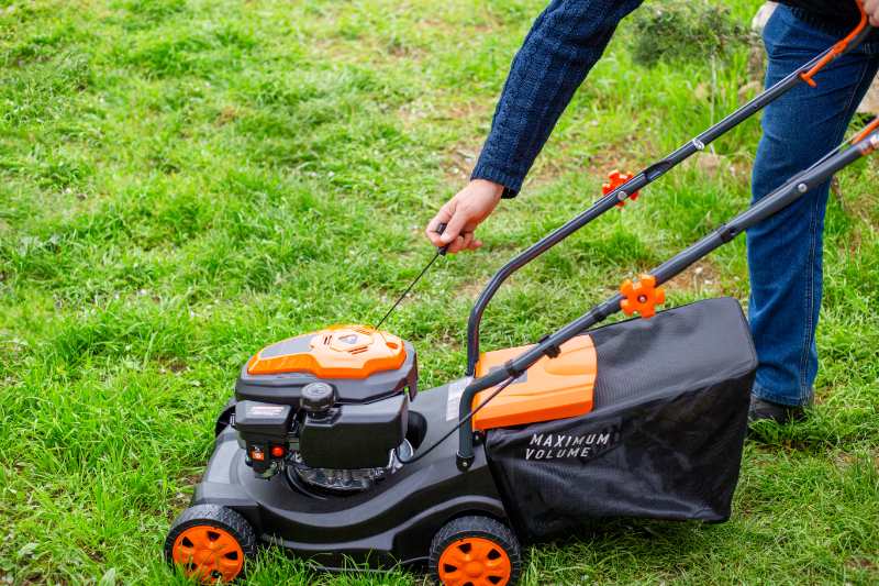 A man starting the engine of a gas lawn mower with a starter rope