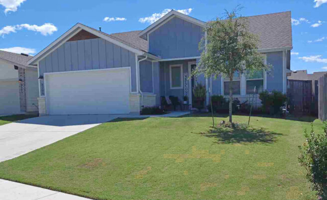 A blue house sits on a hill with a manicured lawn.