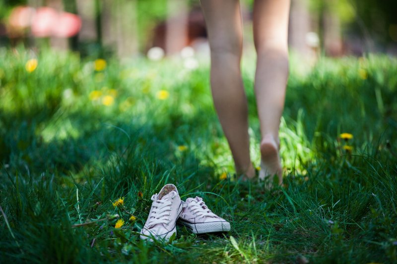Woman walking barefoot on the grass and pink shoes in focus