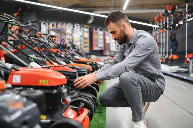 Man examining a row of lawn mowers in a hardware store.