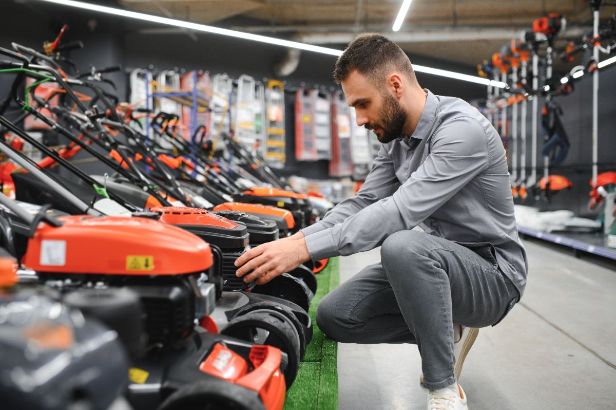 Man examining a row of lawn mowers in a hardware store.
