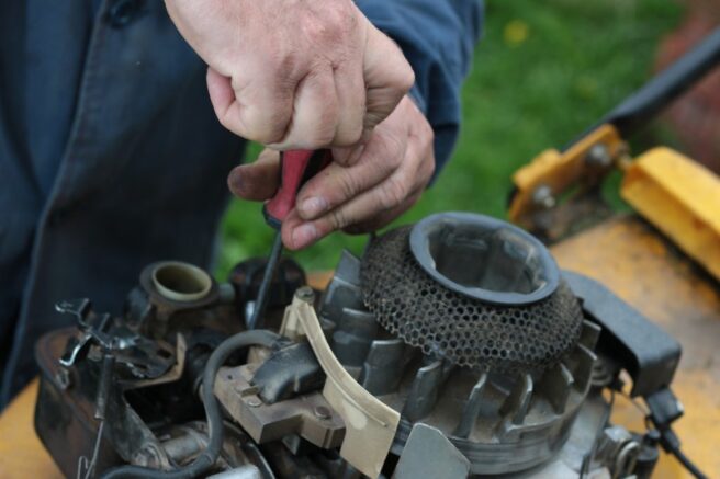 Close-up of hands using a screwdriver to look at a small engine on a lawn mower.