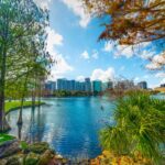 Lush green grass surrounds a lake with trees and the skyline of orlando in the background in springtime.
