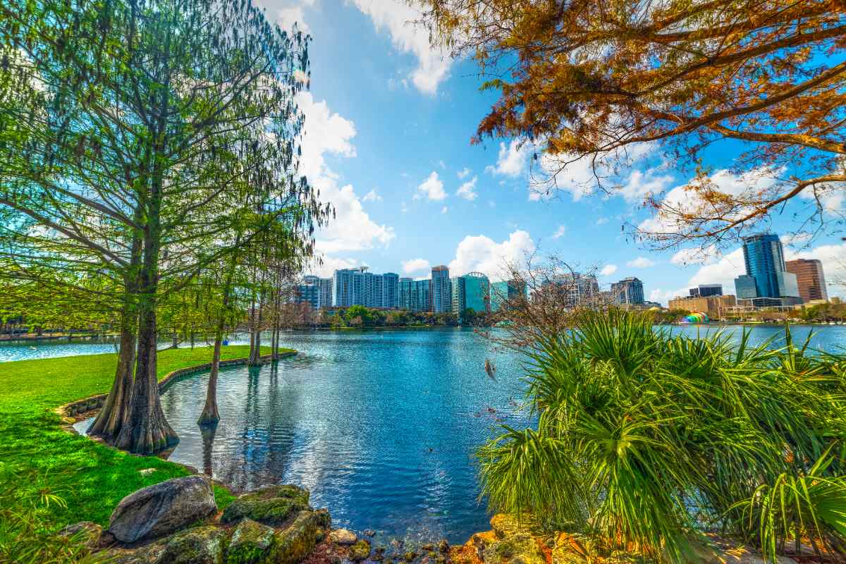 Lush green grass surrounds a lake with trees and the skyline of orlando in the background in springtime.