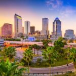 Skyline of Tampa, FL, with palm trees at dusk.