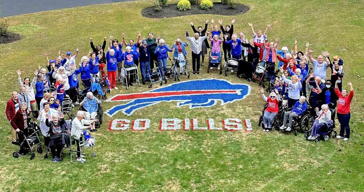 A bunch of people stand around a lawn painting of the Buffalo Bills logo with the text "Go Bills!" underneath of the logo.