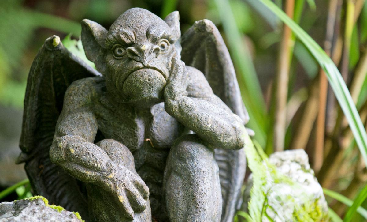 A cement gothic gargoyle has a puzzled look on its face in a garden.