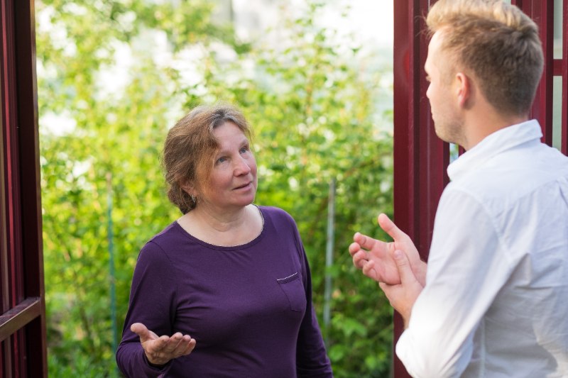 Woman and man having a calm conversation outdoors near a doorway, discussing neighborly issues and resolving a dispute about yard leaves.