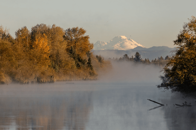 Mist rises from the Snohomish River in Washington with mountains in the distance