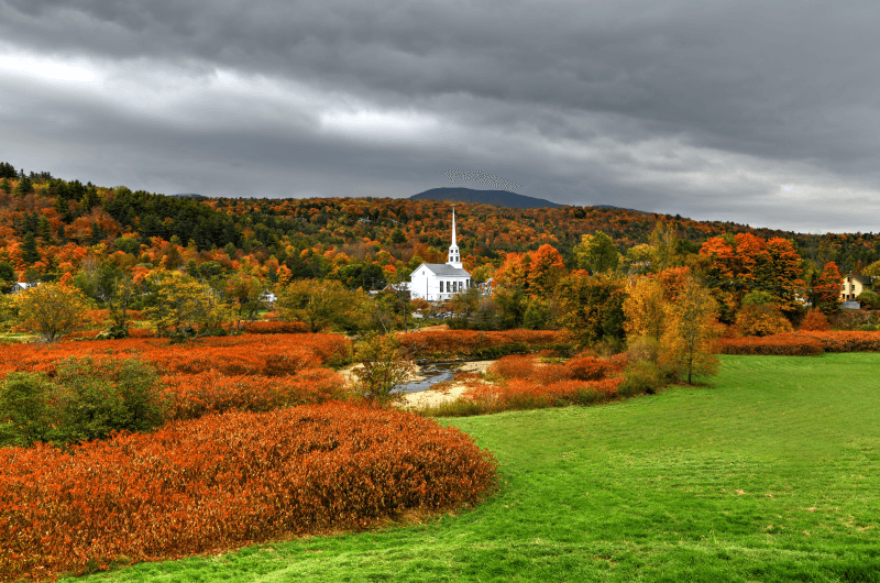 Orange, yellow, green, and brown trees pop around a white church in Stowe, Vermont
