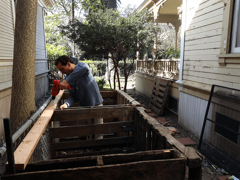 A person builds raised compost bins in a small residential alleyway in Los Angeles