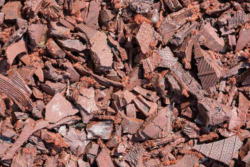 Close-up of shredded rubber mulch pieces in reddish brown tones, forming a rough, springy ground cover texture in a dense layer.