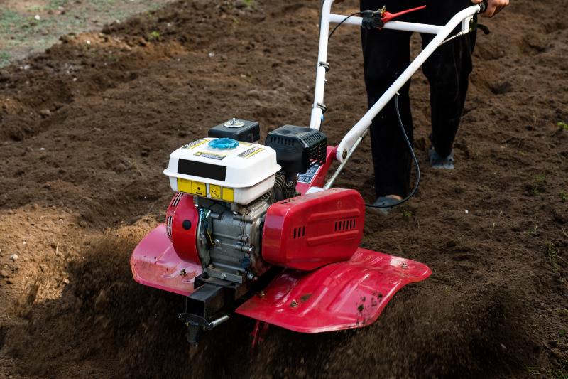 Man working in the garden with garden tiller machine