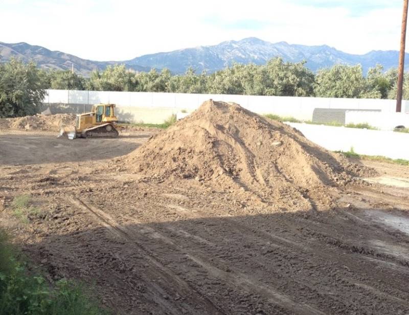 Large yard during lawn renovation with leveling mix, showing soil piles, bulldozer, fenced perimeter, and mountains before golf course-style turf.