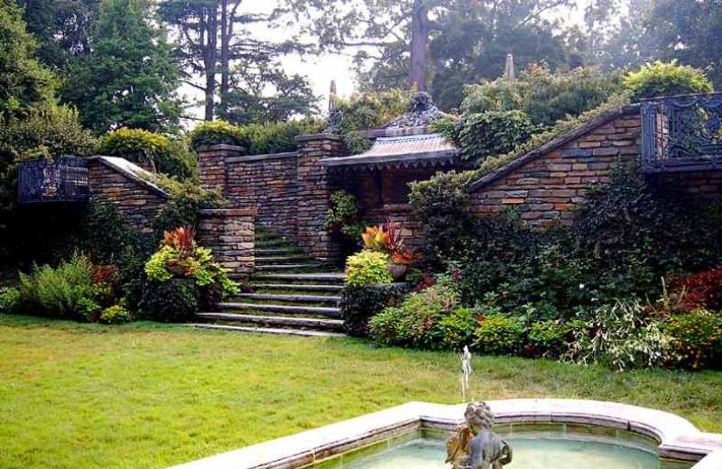 Terraced stone garden at Dumbarton Oaks features central steps, layered plantings, elevated walls, and a small fountain before tall trees.