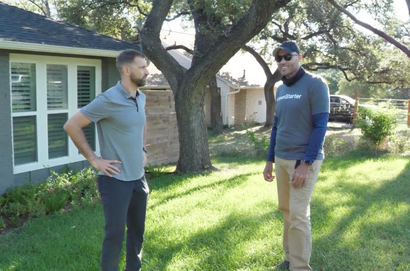 LawnStarter pro Justin Stultz talks with a homeowner in a shaded front yard after completing residential lawn care work.